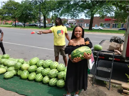 A customer carrying a watermelon away from the truck